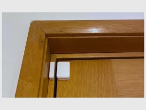 Weißer TTLOCK-TÜRSENSOR mit Sensorelement und Magnet nebeneinander an einer Holztür und am Türrahmen montiert.